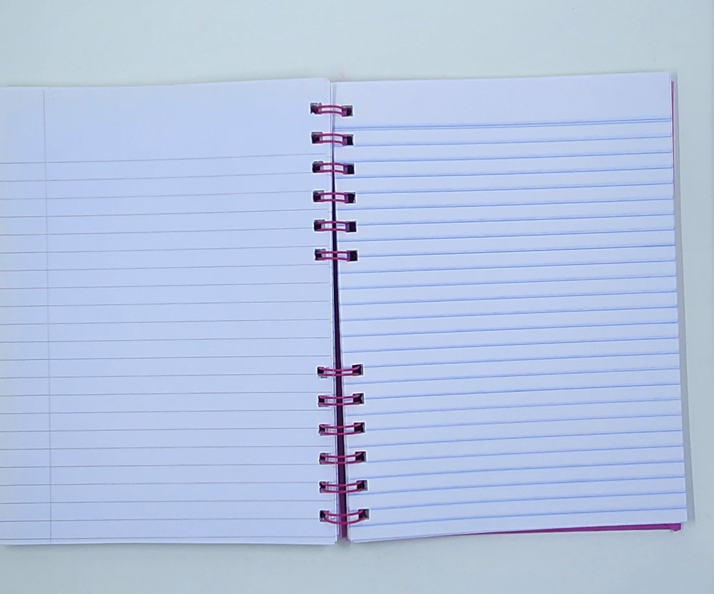 Open notebook with lined pages and a pink spiral binding on a light background
