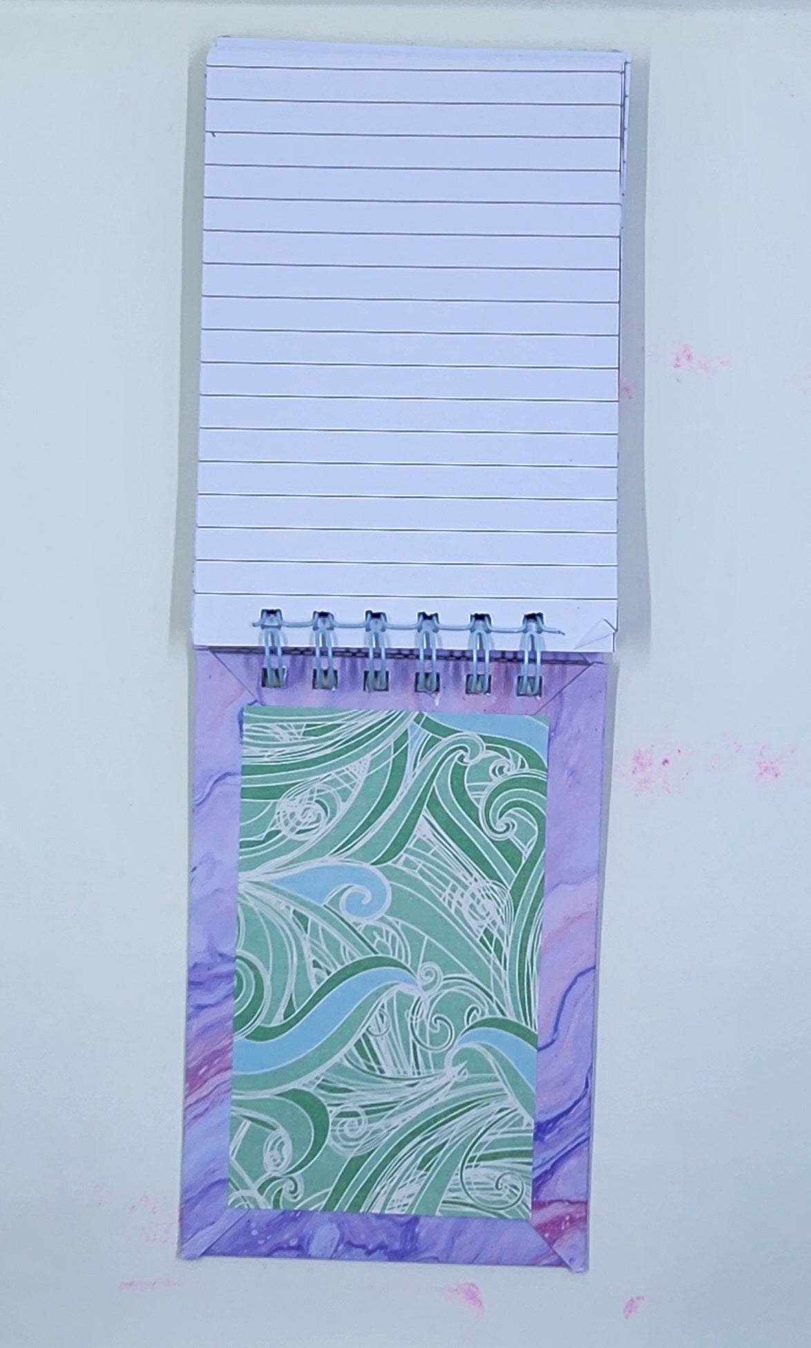 Notepad with lined pages and a decorative purple back cover on a white background