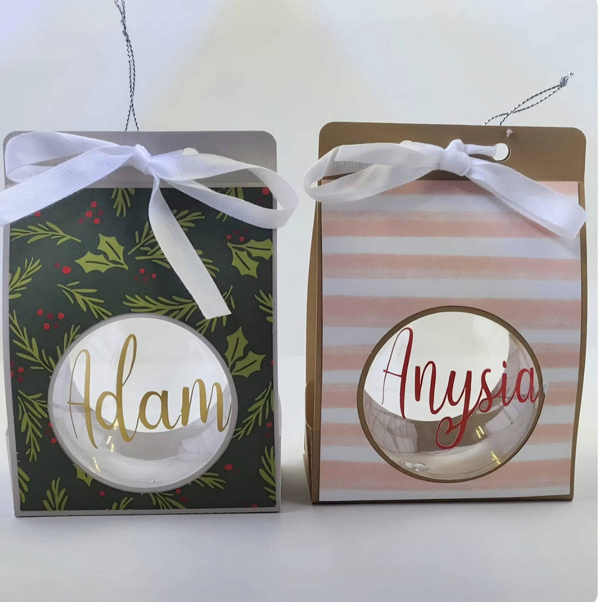 Two personalised clear Christmas baubles with the names Adam in gold and Anysia in red, in handmade gift boxes with white ribbons