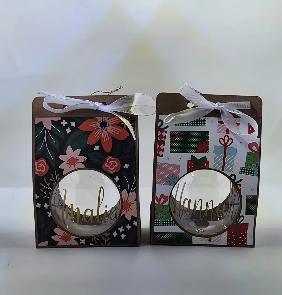 Clear Christmas baubles personalised with the names Amalia and Hannah in gold lettering, in festive gift boxes