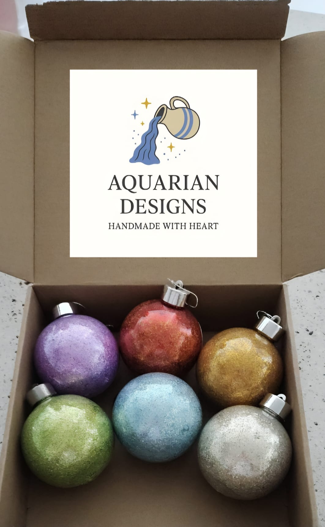 Six glitter-filled Christmas baubles in purple, red, gold, green, blue and silver, in an Aquarian Designs box