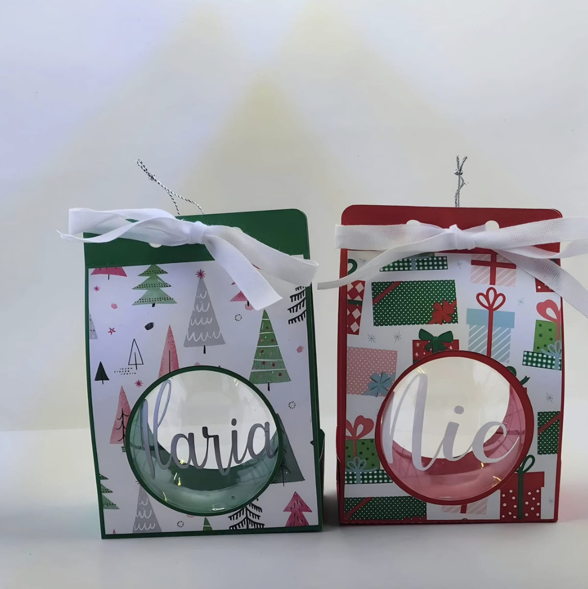 Two personalised clear Christmas baubles with silver and white name lettering, in green and red patterned gift boxes