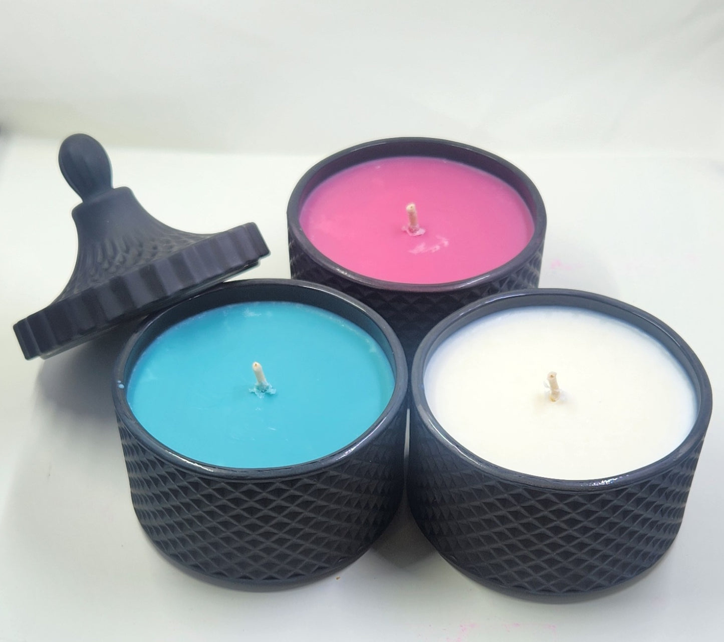 Three scented candles in black containers with different coloured wax on a white background