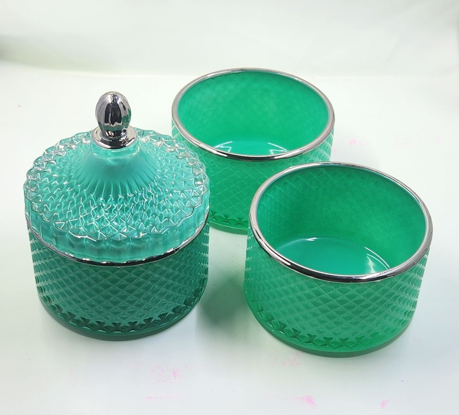 Set of three green glass containers with textured design and silver rims on a white background