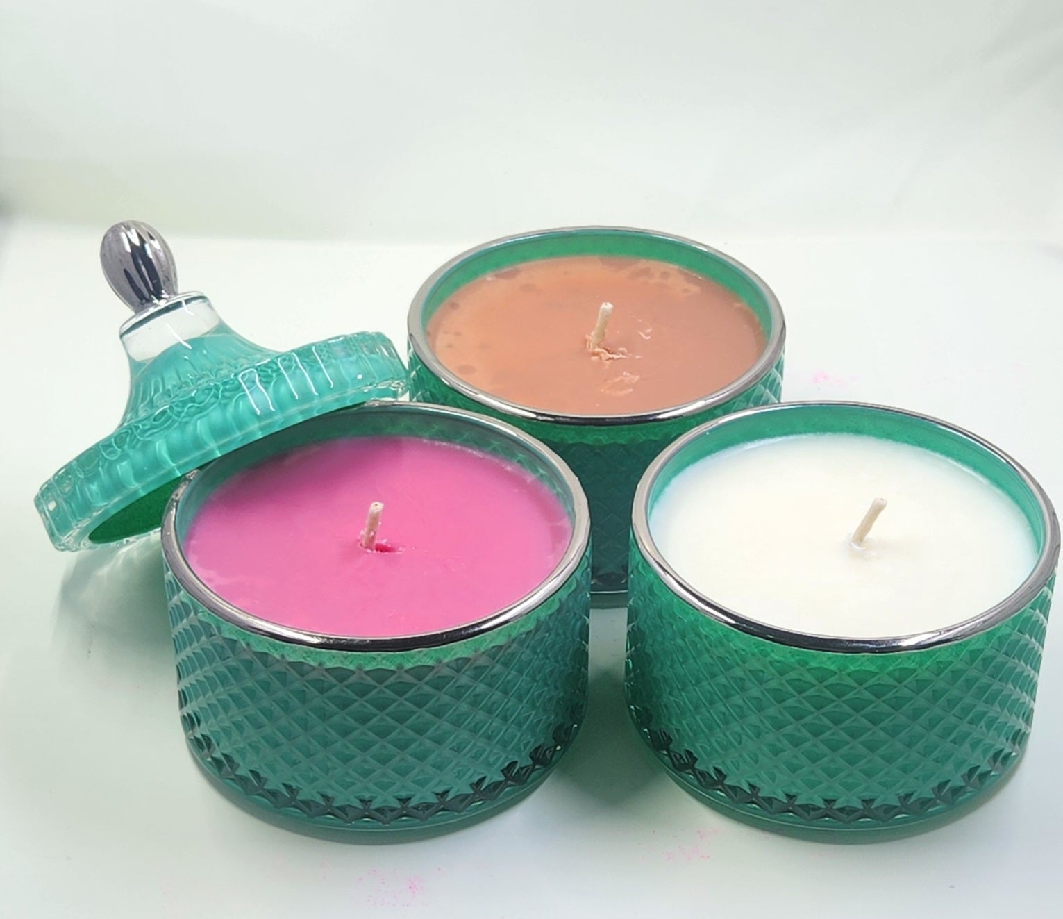 Three teal textured candle holders with pink, brown, and white candles on a white background