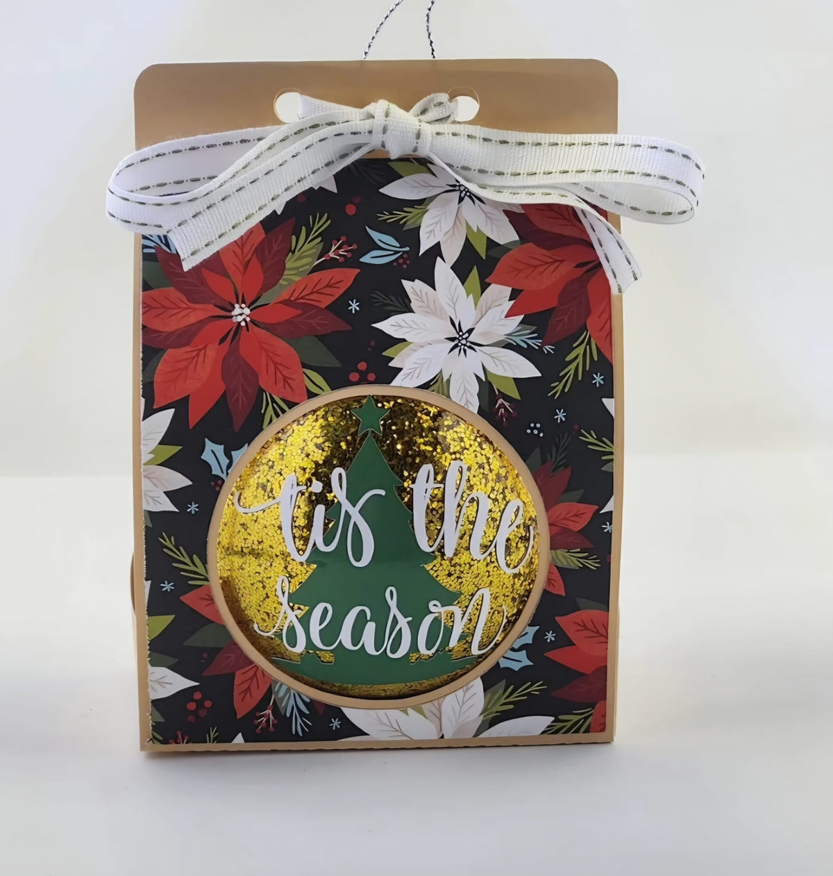 Gold glitter Christmas bauble with a "Tis the season" greeting and green tree design, in a poinsettia gift box