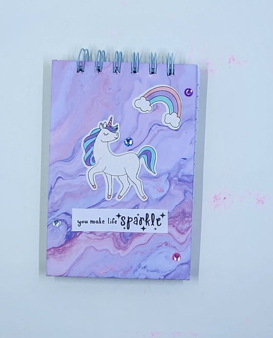 Notebook with a unicorn design and 'you make life sparkle' text on a white background. 