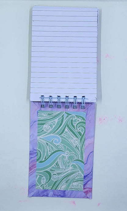 Notepad with lined pages and a decorative purple back cover on a white background